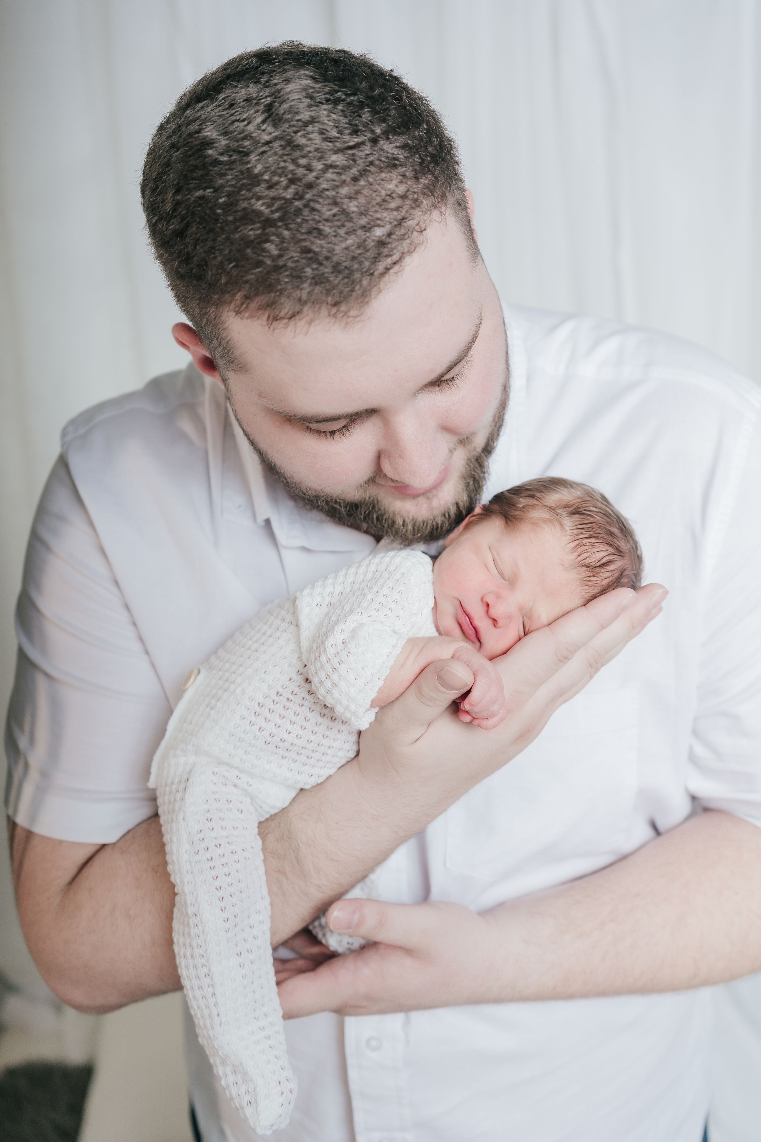 Parent cradling sleepy newborn wearing white knit clothing.