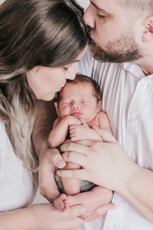 Intimate family portrait with newborn baby held close between parents.