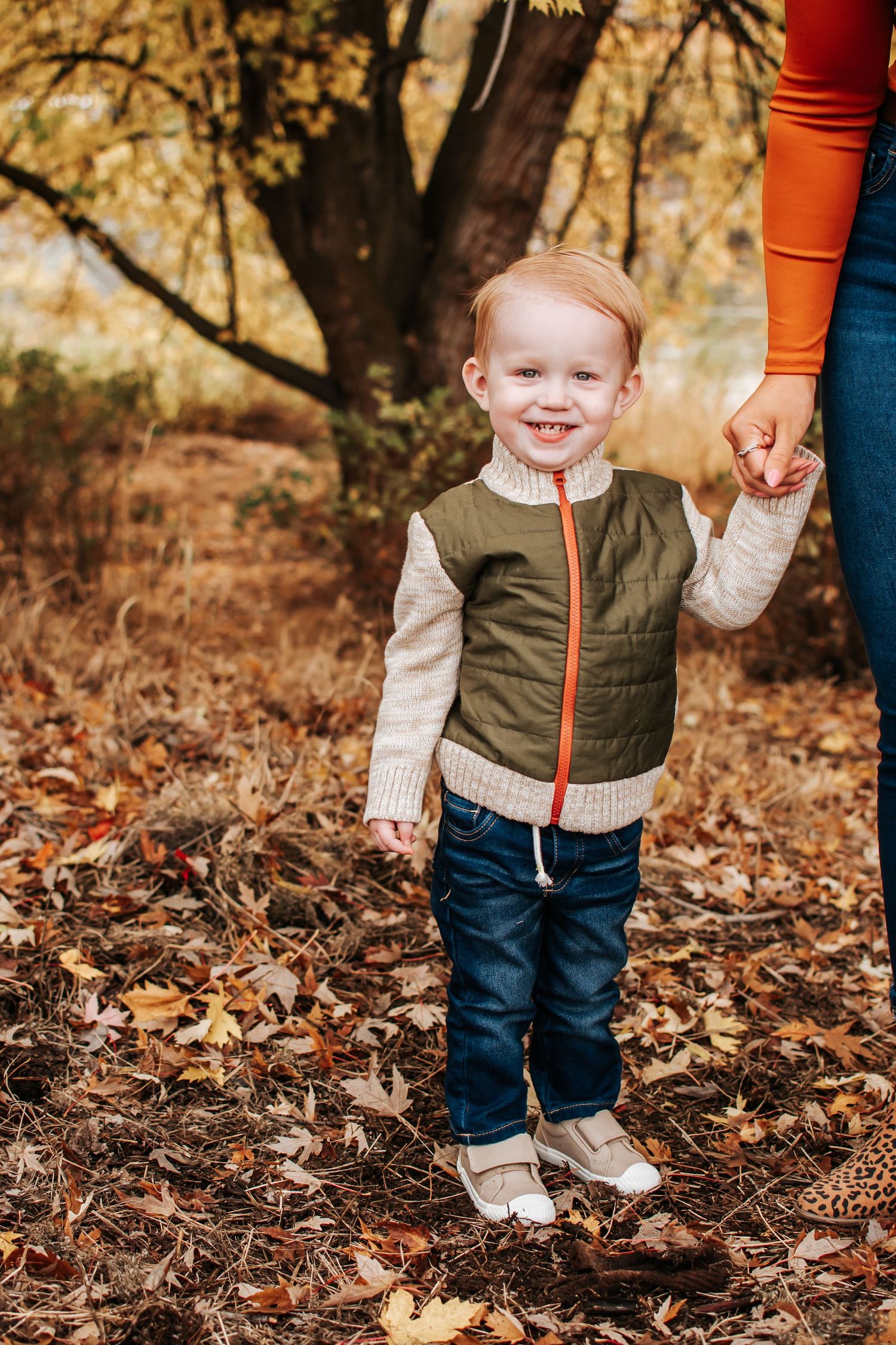 Small child in olive vest and sweater standing on fall leaves at Chamna Natural Preserve in Richland, Washington.