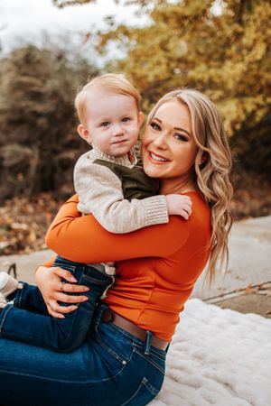 A mom in an orange top holds a small child wearing a beige sweater during a fall outdoor photoshoot in Richland, Washington.
