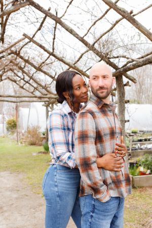 Couple embracing under wooden pergola surrounded by winter trees.