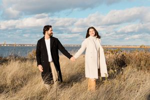 A couple embraces in tall golden grass against a cloudy sky during a romantic photoshoot by Hamptons photographer.