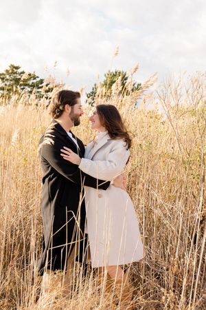 Playful couple in black and white outfits dance through a field of tall grass by Hamptons photographer.