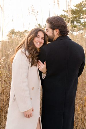 Couple laughs together while posing in a field of dried grass during golden hour by Hamptons photographer.
