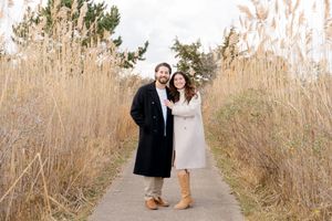 Couple walks hand in hand through a scenic path lined with tall grass by Hamptons photographer.
