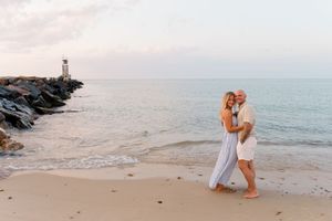 Emotional beach proposal moment with waves and rocky jetty in background by Hamptons photographer.