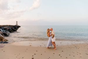 A surprise beach proposal captured during golden hour with lighthouse in background by Hamptons photographer.