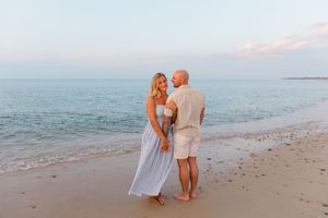 A romantic beach photoshoot at sunset with two people embracing on the sandy shore by Hamptons photographer.