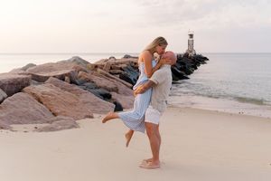 A beachside proposal scene with two people on the sand near rocky formations by Hamptons photographer.
