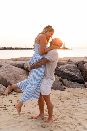 Two people sharing an intimate moment on a beach with rocks and ocean in the background by Hamptons photographer.