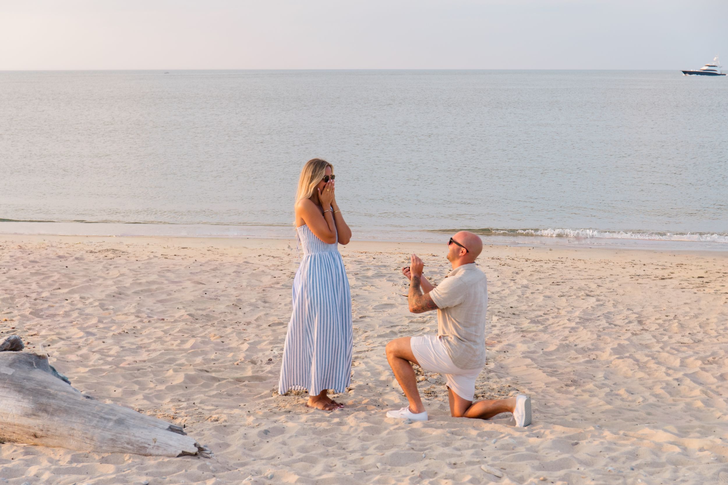 A romantic beach proposal scene with someone kneeling on the sand by Hamptons photographer.