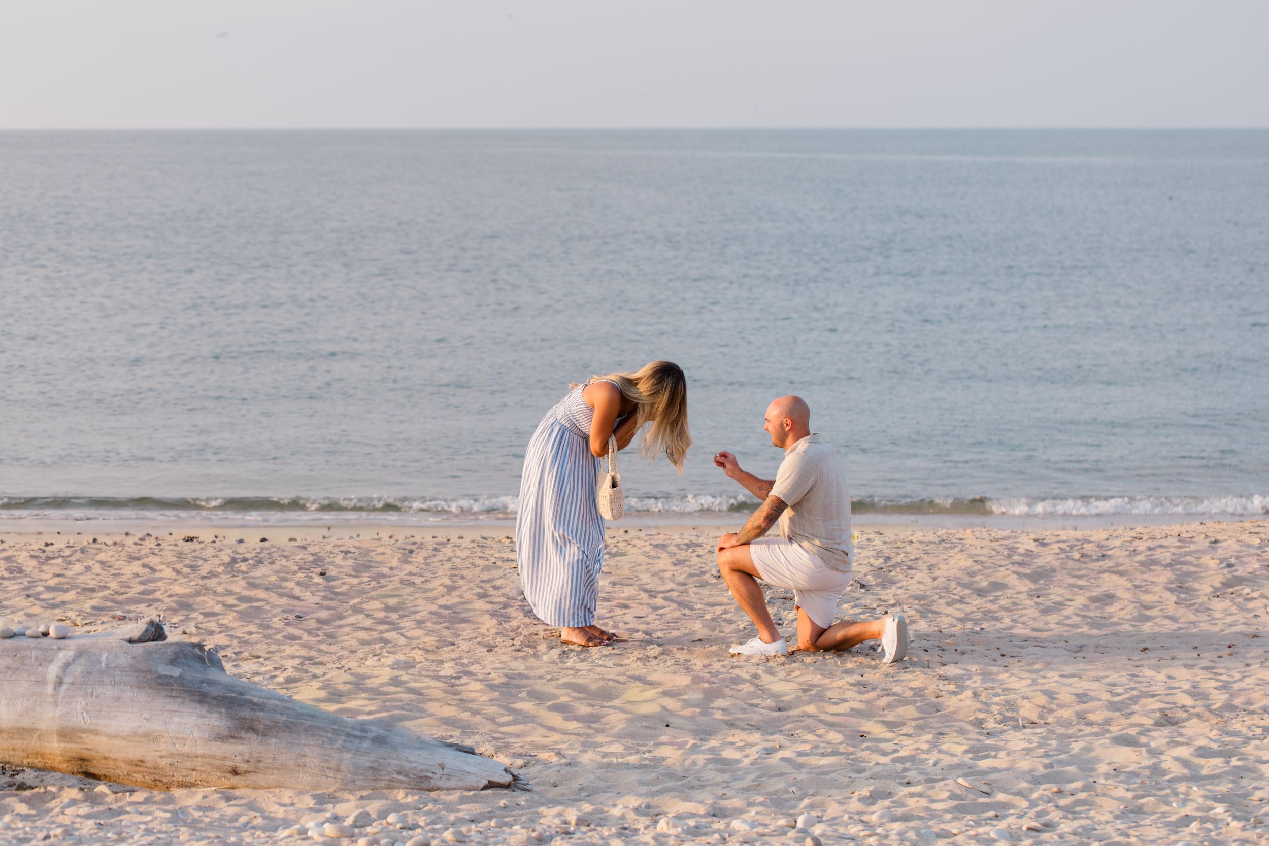 Family enjoying a playful moment together on a sunny beach with waves in the background by Hamptons photographer.