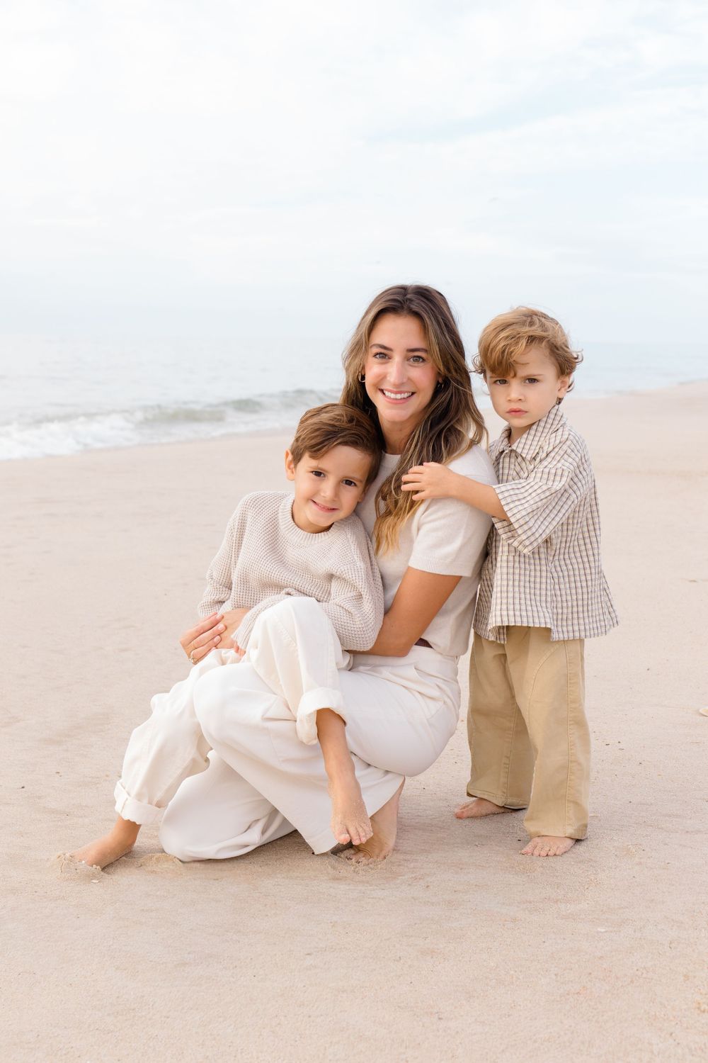 A casual beach portrait of a parent and two children sitting in the sand.