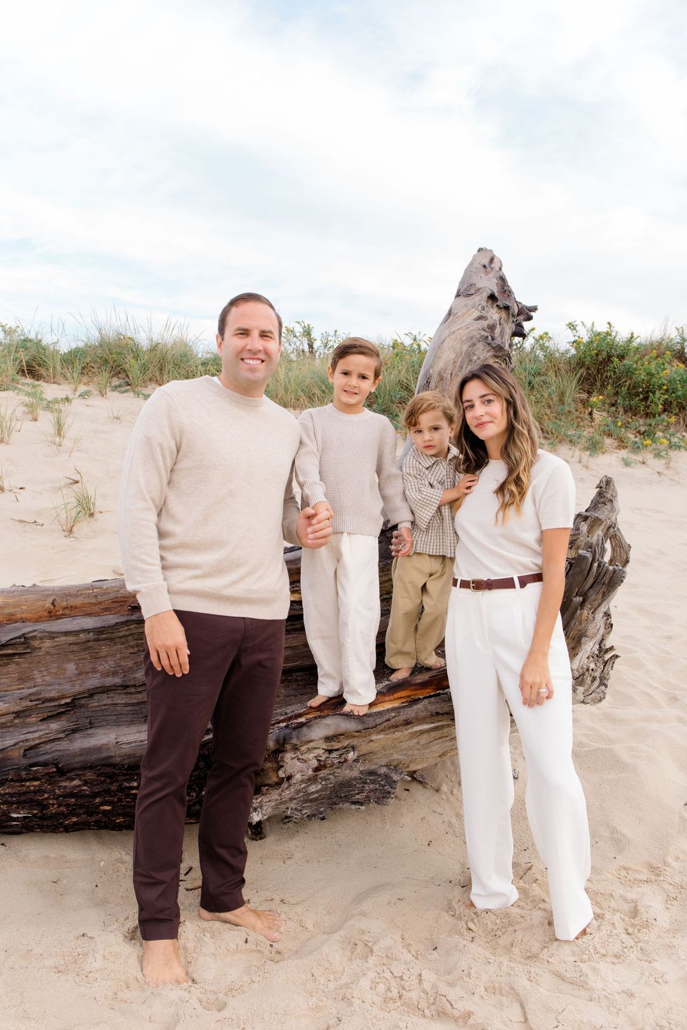 A family poses together on a beach with driftwood and sand dunes in the background.