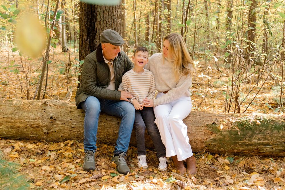 Family sitting together on a log in a golden autumn forest setting.