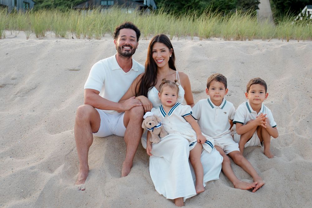 Family enjoying a playful moment together on beach in white summer attire.