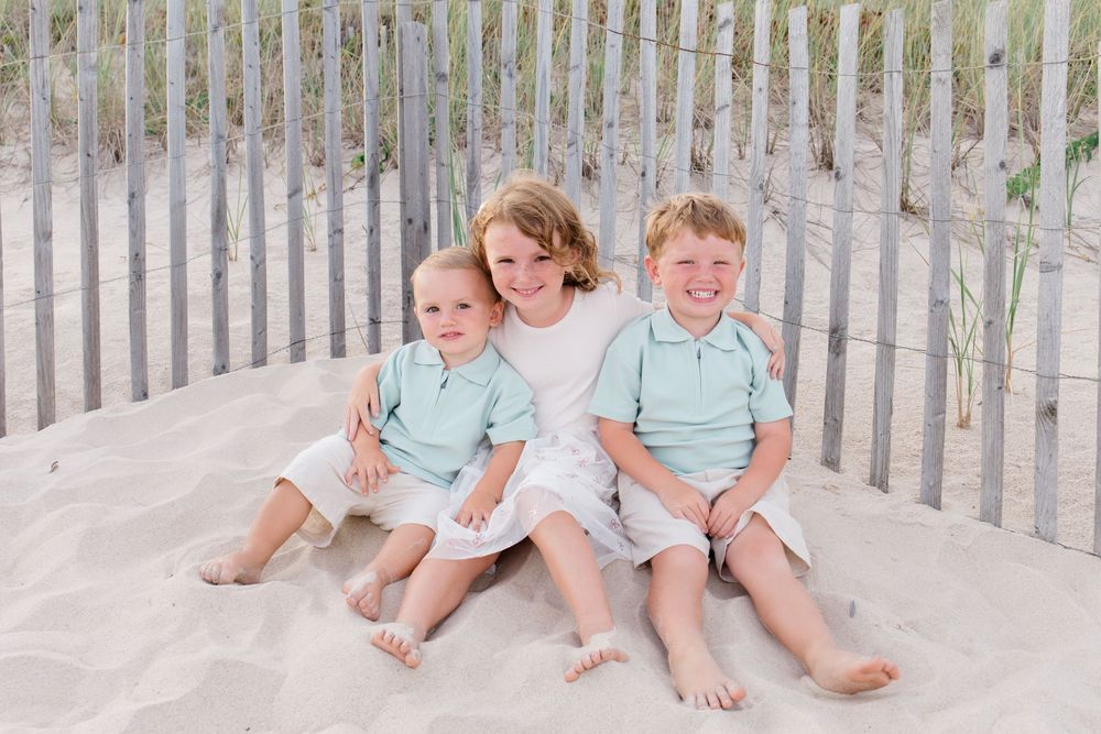 Casual family portrait on beach with wooden fence and dunes in background.