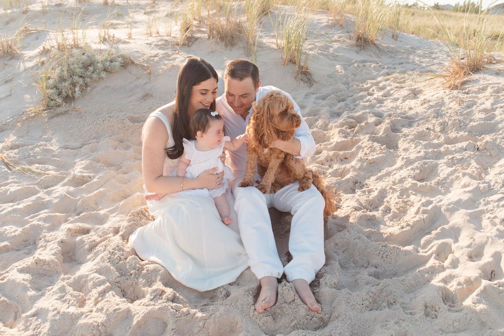 Family relaxing together on sandy beach with their golden retriever dog.