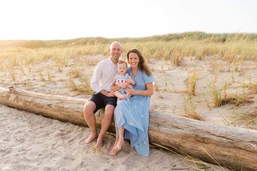 Family sitting together on driftwood at the beach during sunset.
