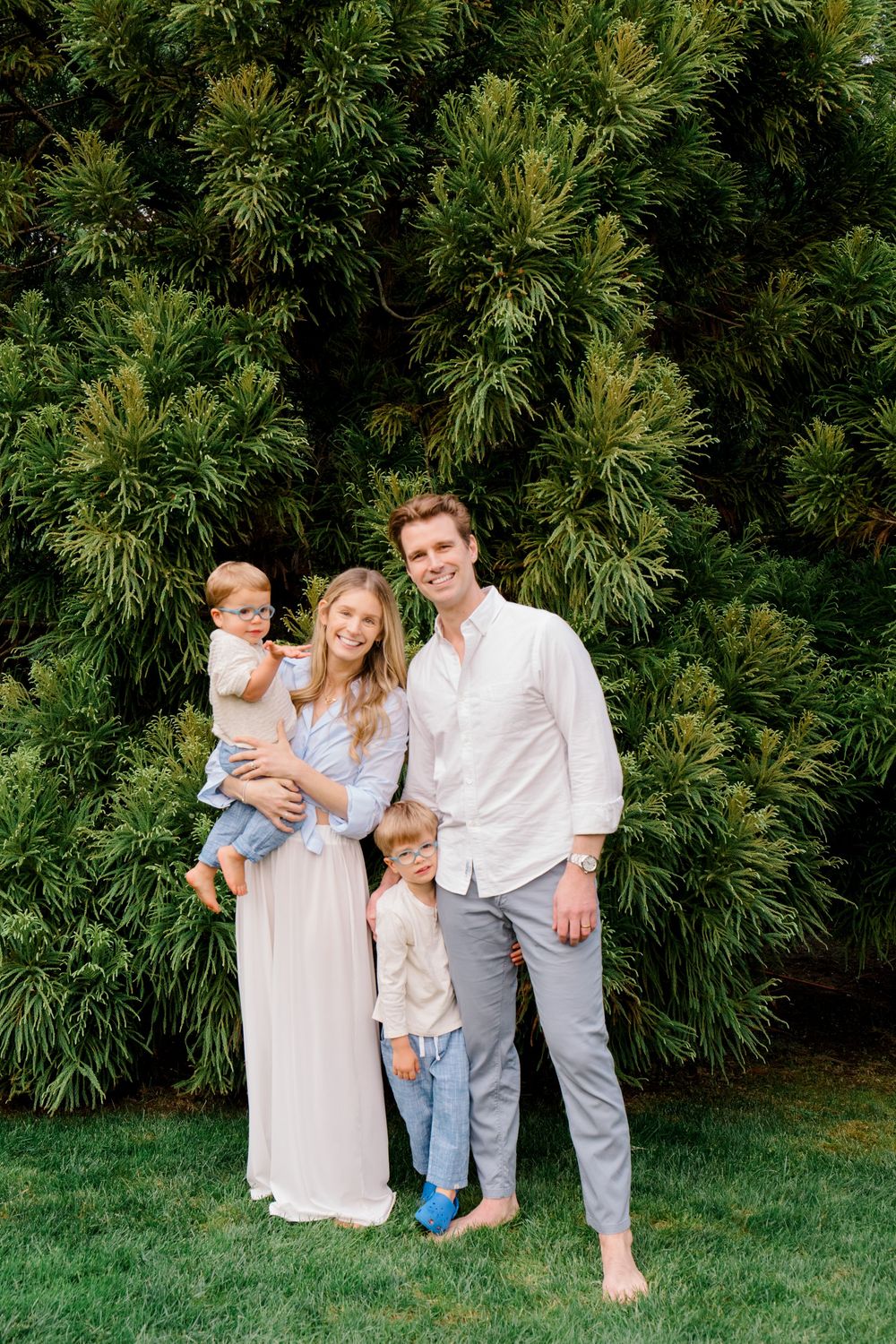 Family in coordinated outfits poses together against a backdrop of evergreen trees.