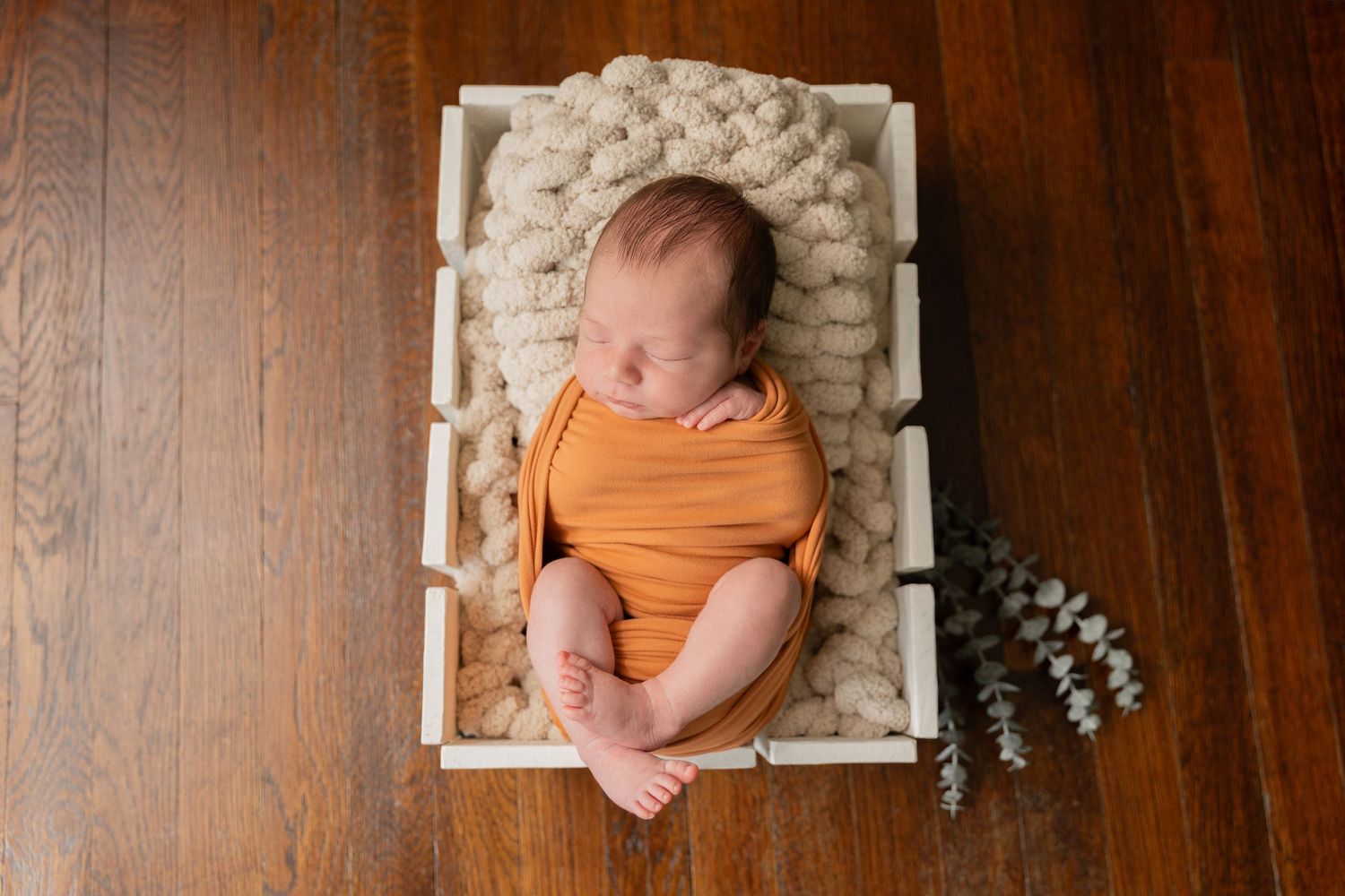 newborn baby boy wrapped in an orange swaddle huck finn