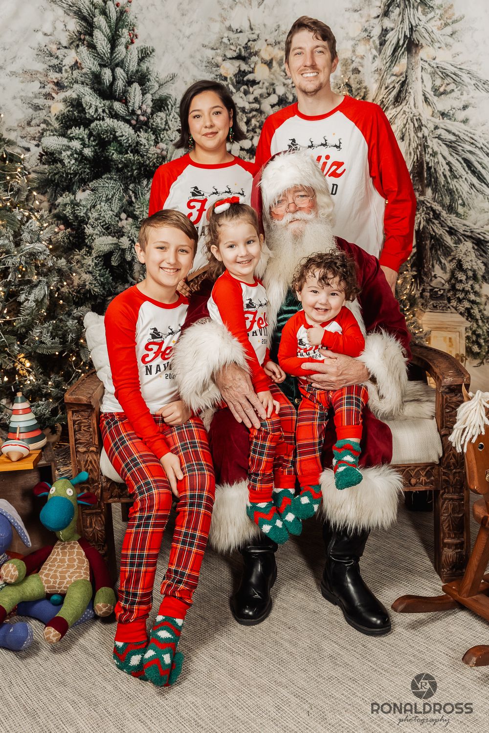 A Christmas photo session with matching red and plaid outfits in front of a decorated evergreen tree and festive backdrop. Santa  Webster
