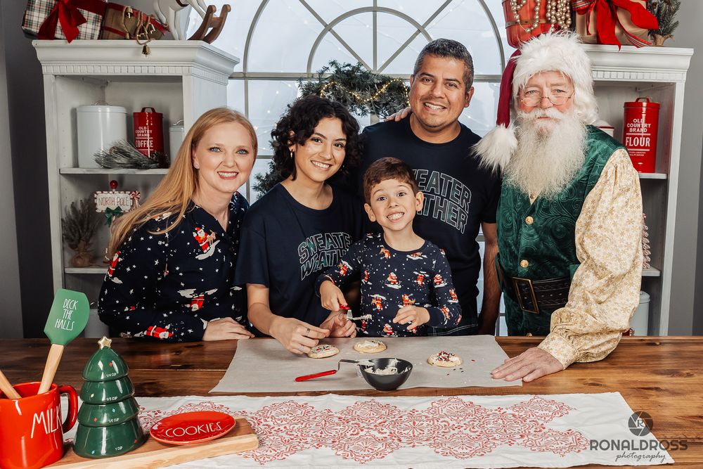 A group of people gathered around a long table decorated for Christmas with red and white patterns and festive decor. Santa Photos Galveston