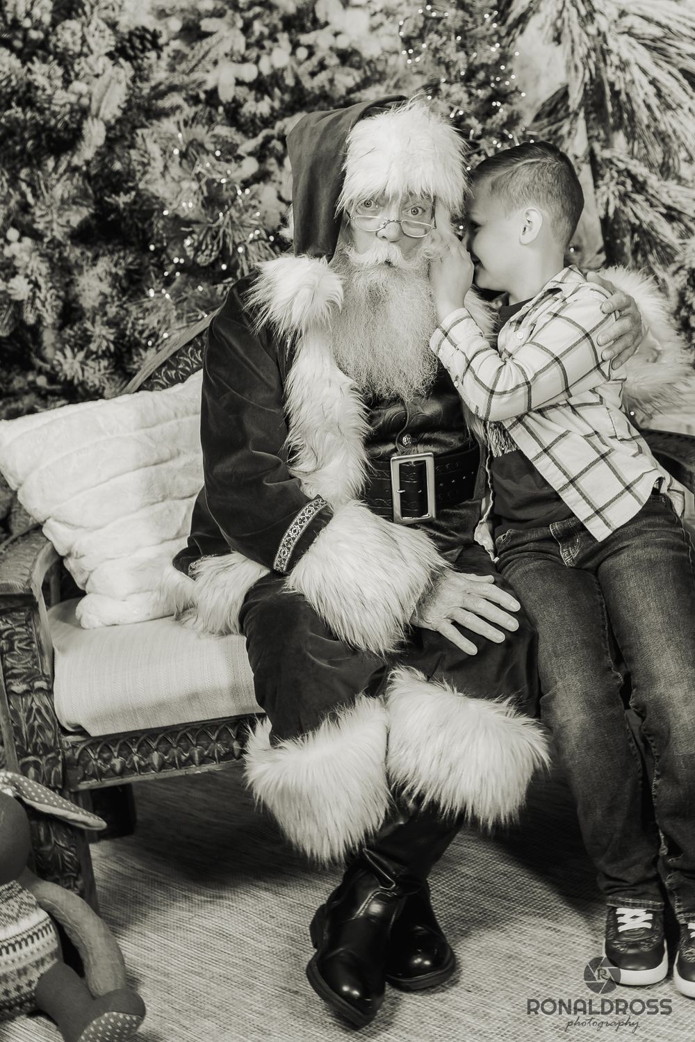 A vintage black and white holiday photo showing a child whispering a Christmas wish while sitting on a festive chair. Santa Photos Galveston
