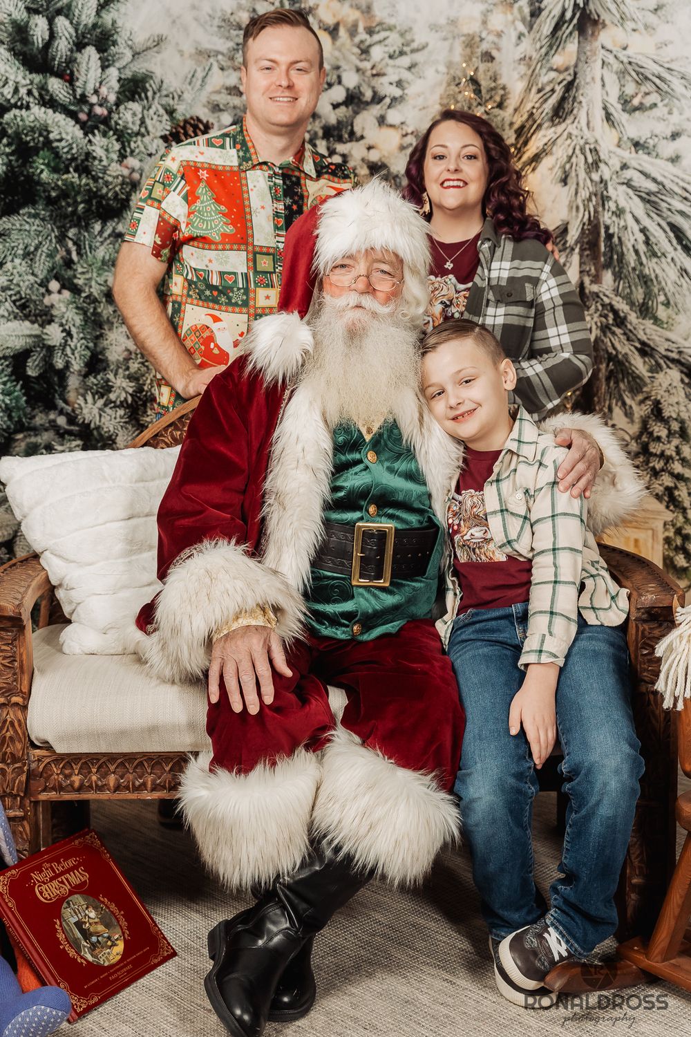 A festive holiday photo series with Santa Claus sitting on a couch surrounded by decorative snowy trees and presents. Santa Photos Galveston