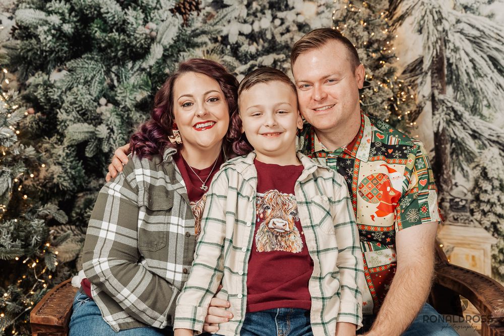A group poses together in front of a decorated Christmas tree wearing coordinating plaid and burgundy outfits. Family Holiday Photos Webster