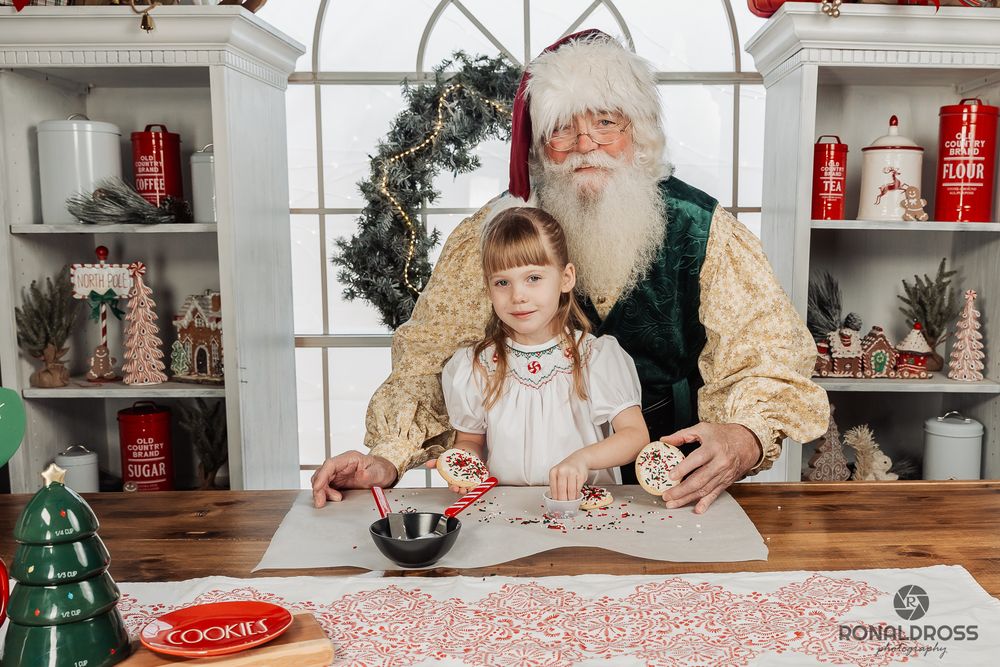 A festive holiday scene with someone baking cookies in a cozy kitchen decorated with Christmas greenery and red accents. Santa Photo Webster