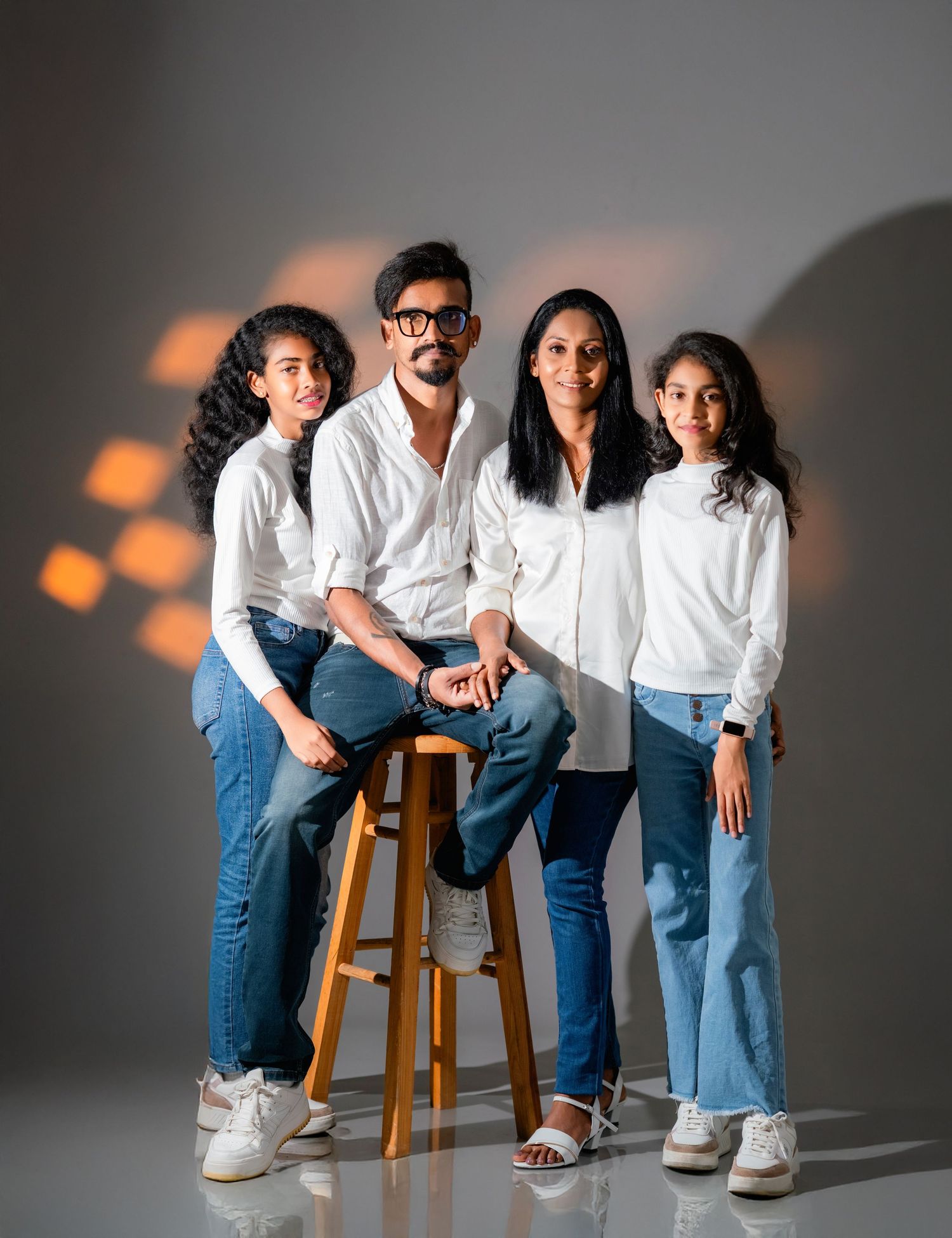 A family group wearing coordinated white shirts and blue jeans poses together against a gray studio backdrop.