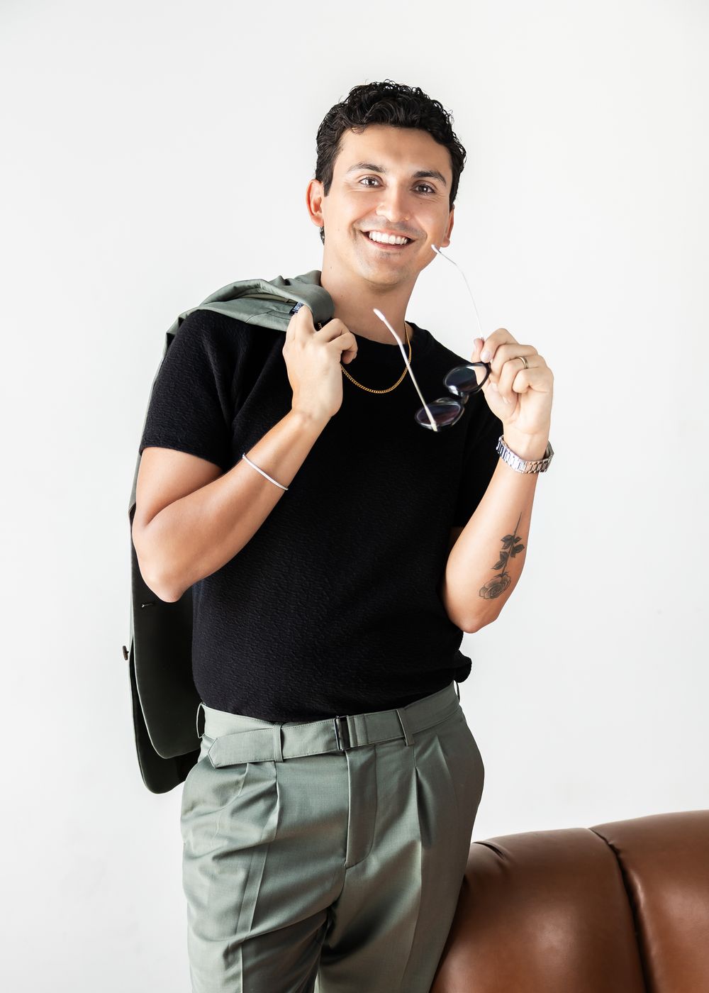 Person wearing black t-shirt and sage green pants poses playfully against brown leather couch in multiple shots.