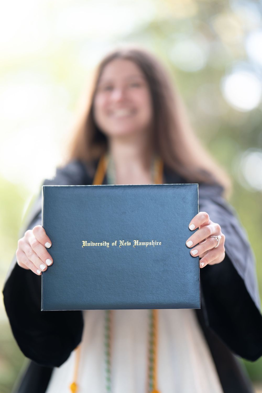 Smiling University of New Hampshire graduate proudly displays her diploma in a navy blue cover.