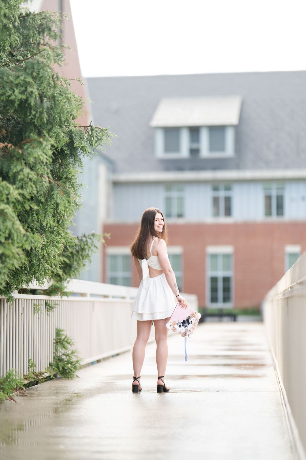 Young woman in white dress holding flowers poses on a wet walkway during a rainy day photoshoot.