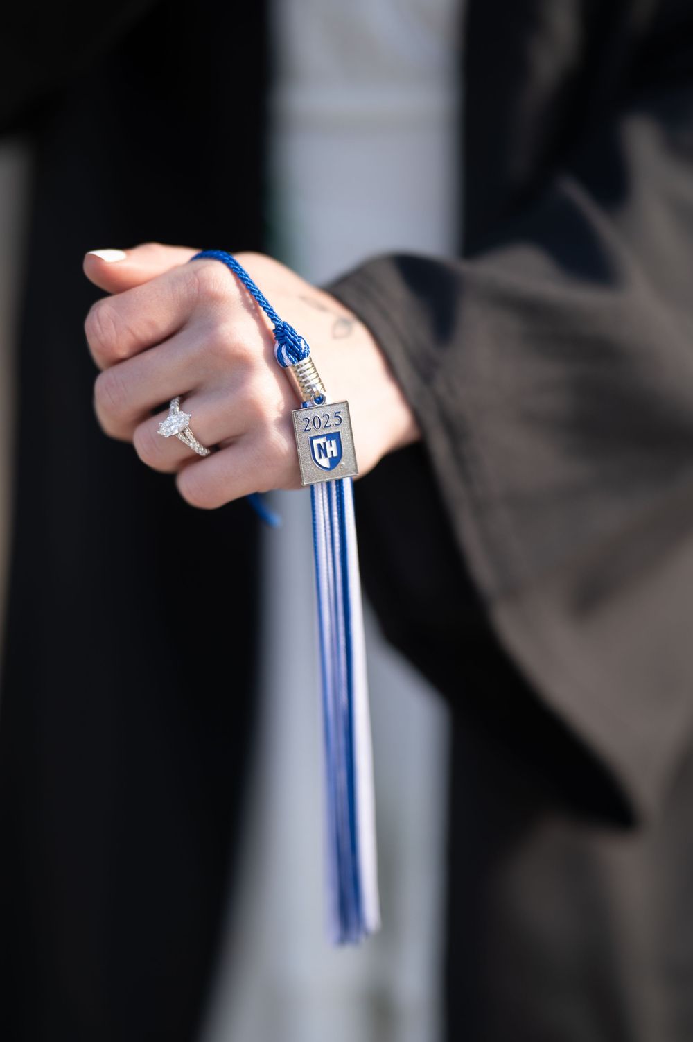 Close-up of a hand holding a 2025 UNH graduation tassel with a blue and silver charm.