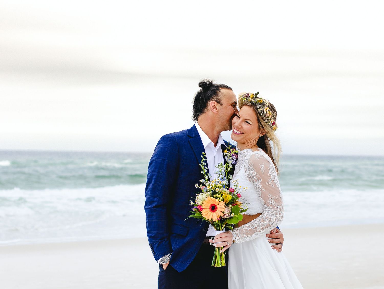 A wedding couple shares an intimate moment on the beach with a colorful bouquet.
