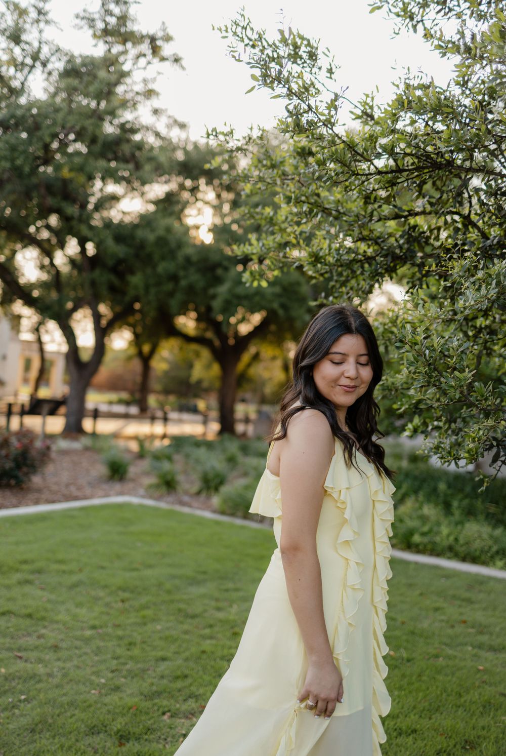 A person in a ruffled yellow dress stands on grass with trees in the background.