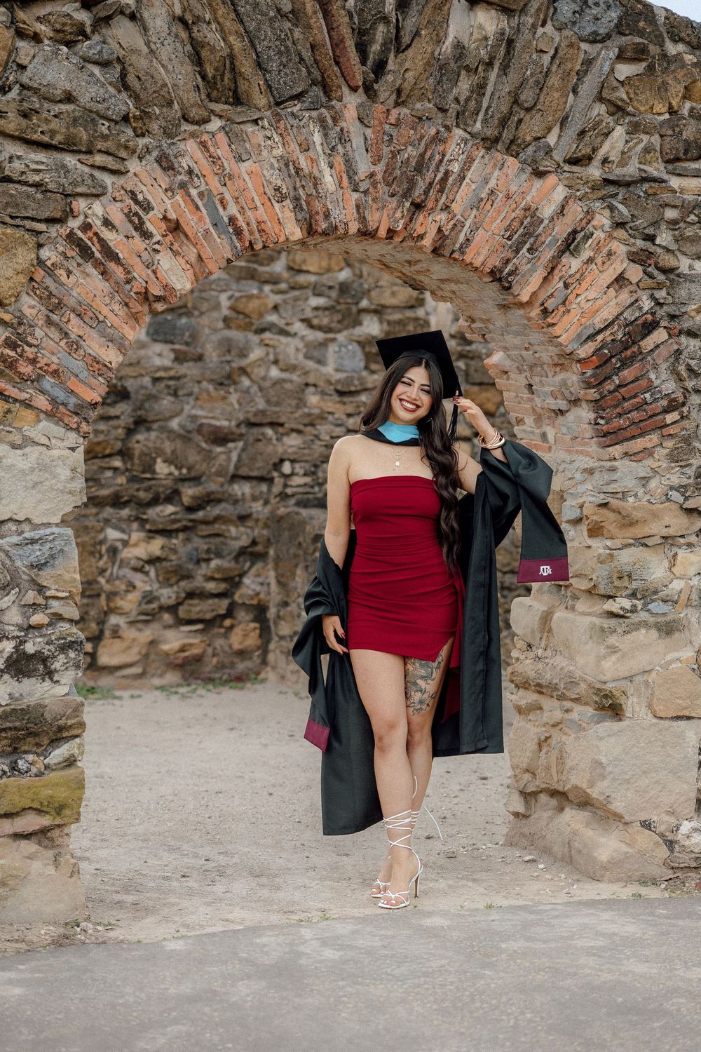 A sequence of photos showing someone in a red dress and black coat posing against a rustic stone archway.