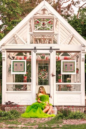White greenhouse structure with decorative windows and red floral accents in a garden setting.