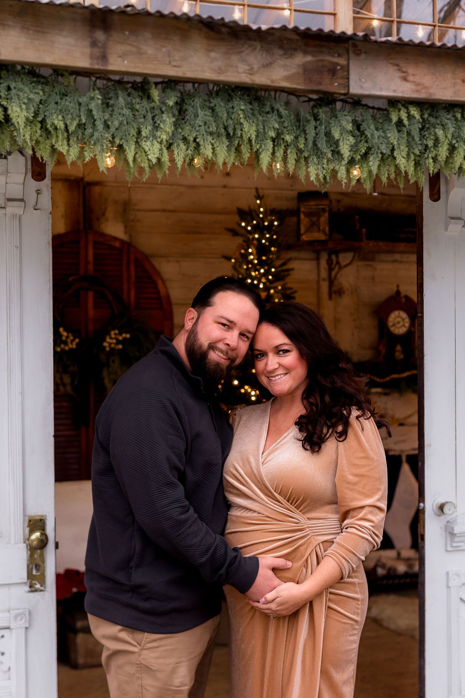 Candid moments captured during a winter maternity session with festive greenery and lights.