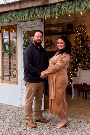 Full-length maternity photos in a rustic setting with holiday decorations and gravel ground.