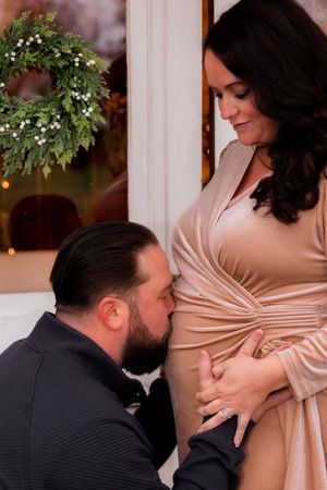 Intimate maternity photoshoot with soft lighting and winter decorations.