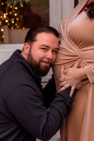Close-up maternity photography with festive evergreen and twinkle light backdrop.