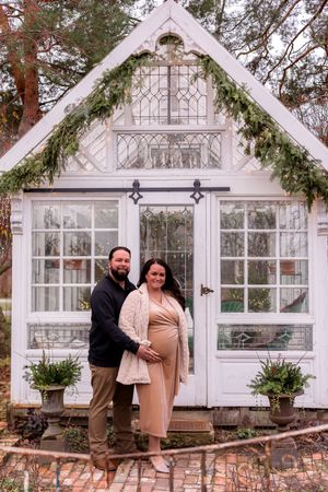 Winter maternity photos in front of a white greenhouse with evergreen decorations.