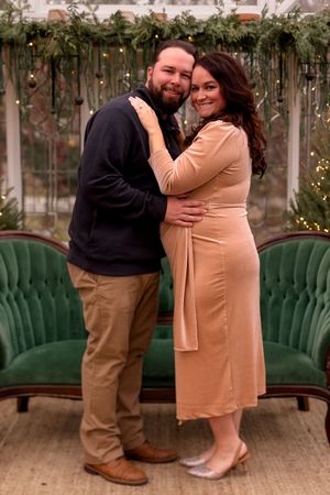 Maternity photo series showing couple in casual attire embracing near emerald green furniture.