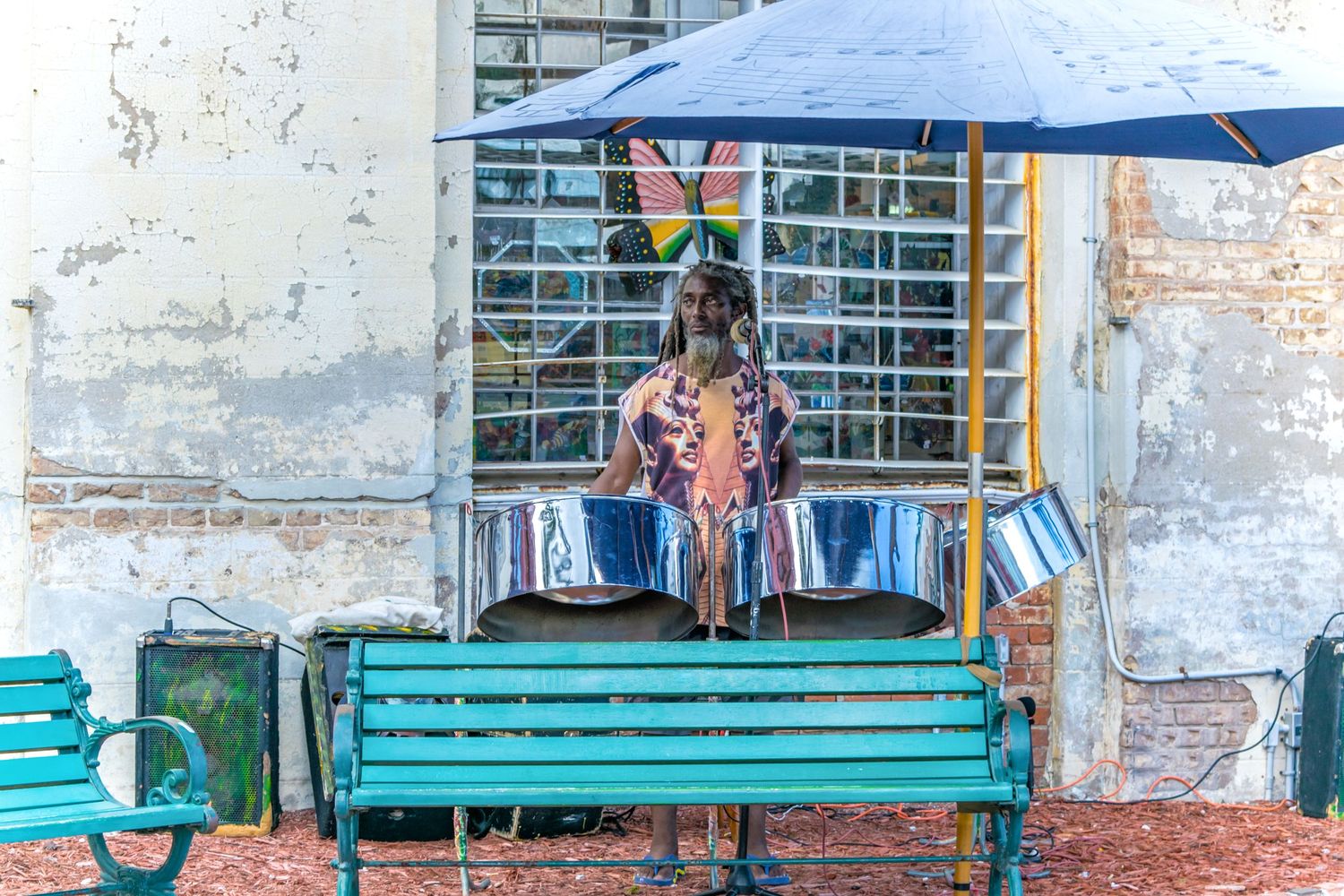 A turquoise bench sits beneath a blue umbrella against a weathered building wall.