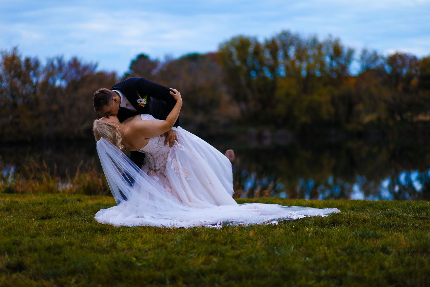 Artistic wedding photography shot with flowing white dress near a lake at sunset.