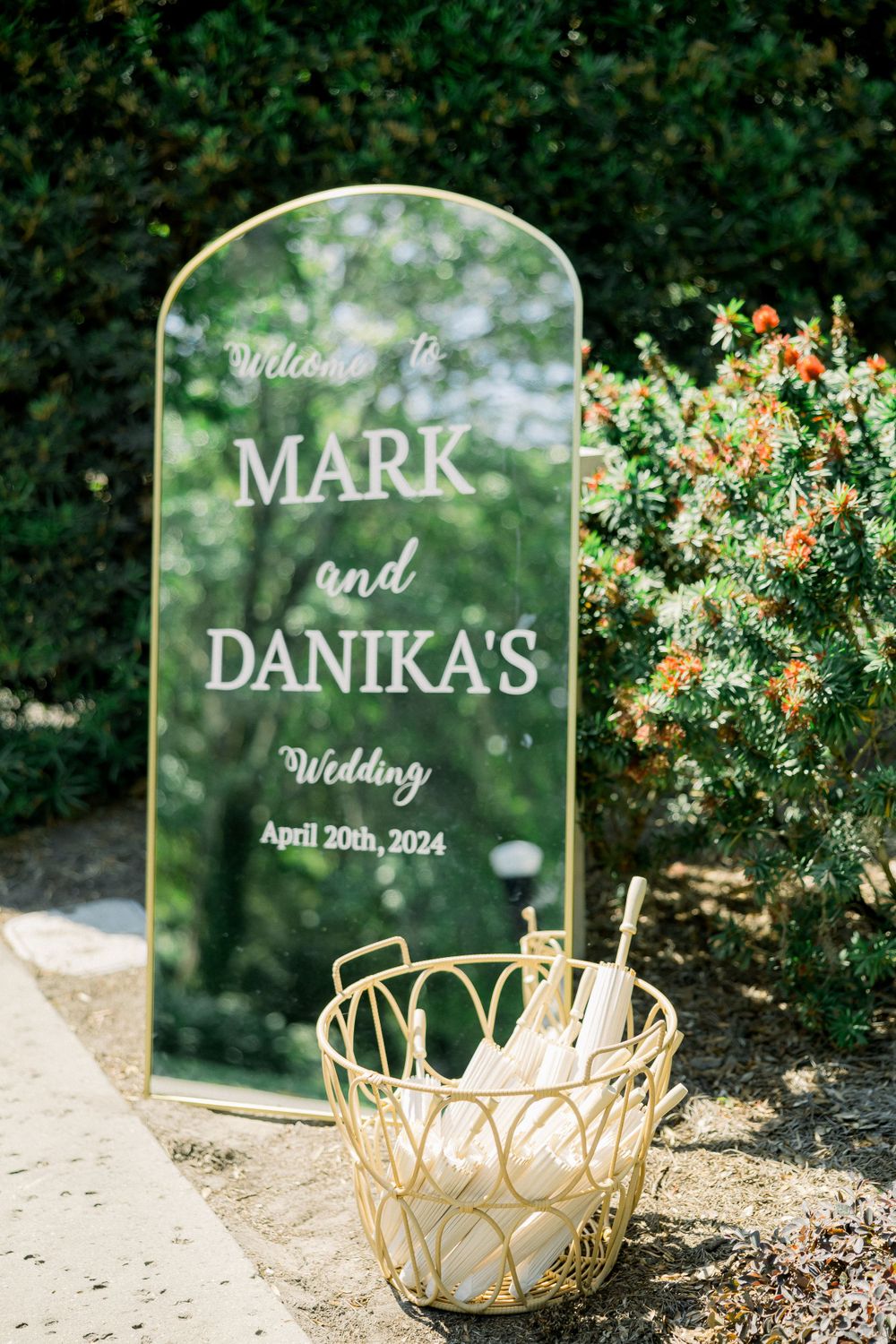 Mirror wedding welcome sign with gold accents and floral decorations in garden setting.