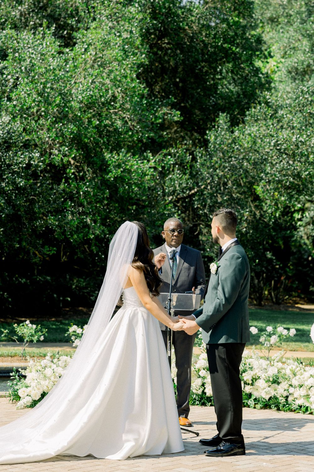 Outdoor garden wedding ceremony with white flowers and greenery backdrop.